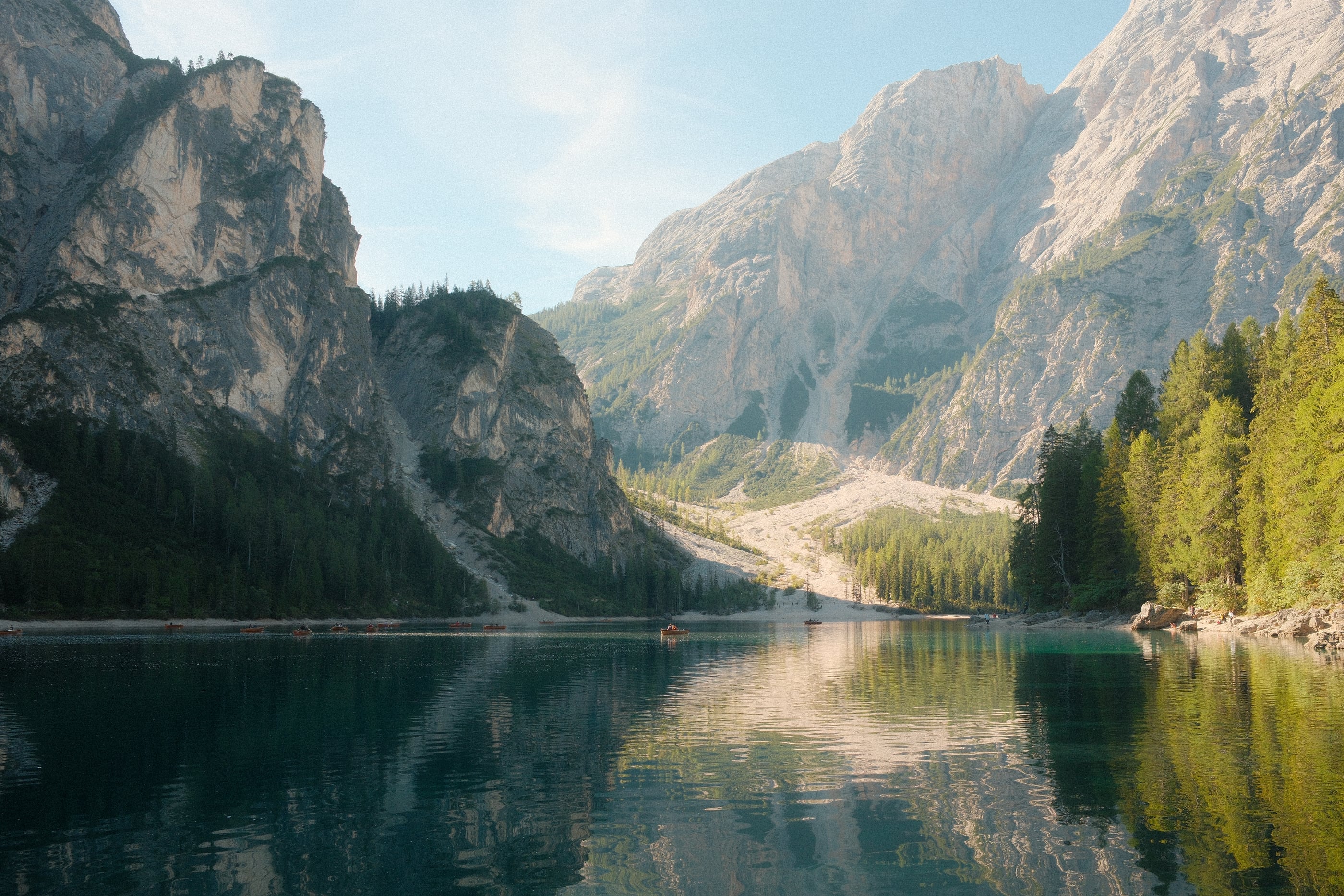 Des falaises et des pentes boisées se reflètent dans l'eau calme et vert sombre du lac, sous un ciel clair.